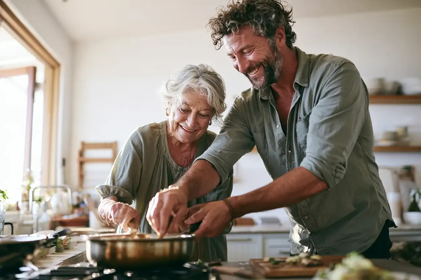 A man in his fifties helping his mother in her eighties in a bright kitchen
