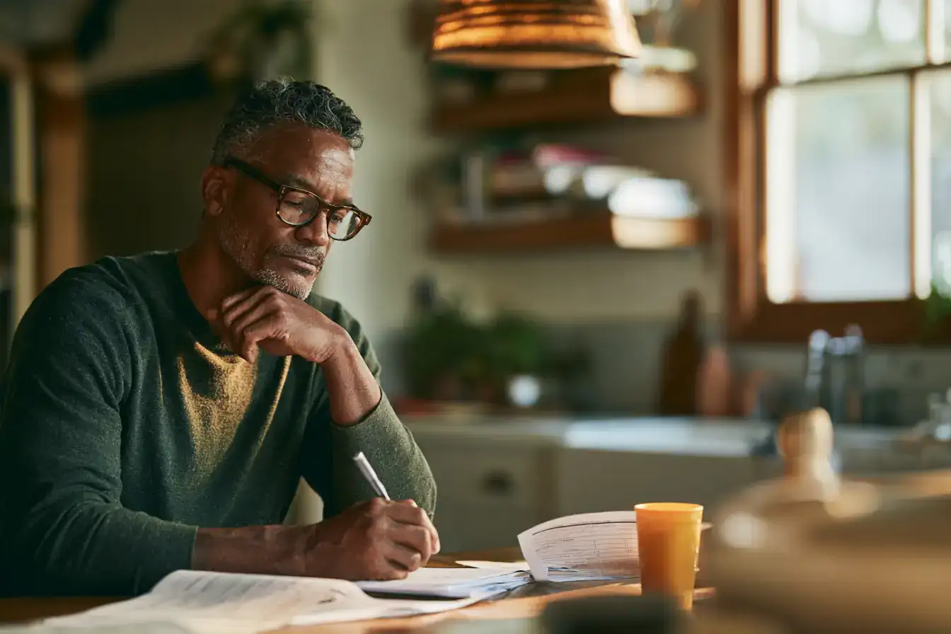 A Black man in his fifties with a printed report and a pen on a kitchen table