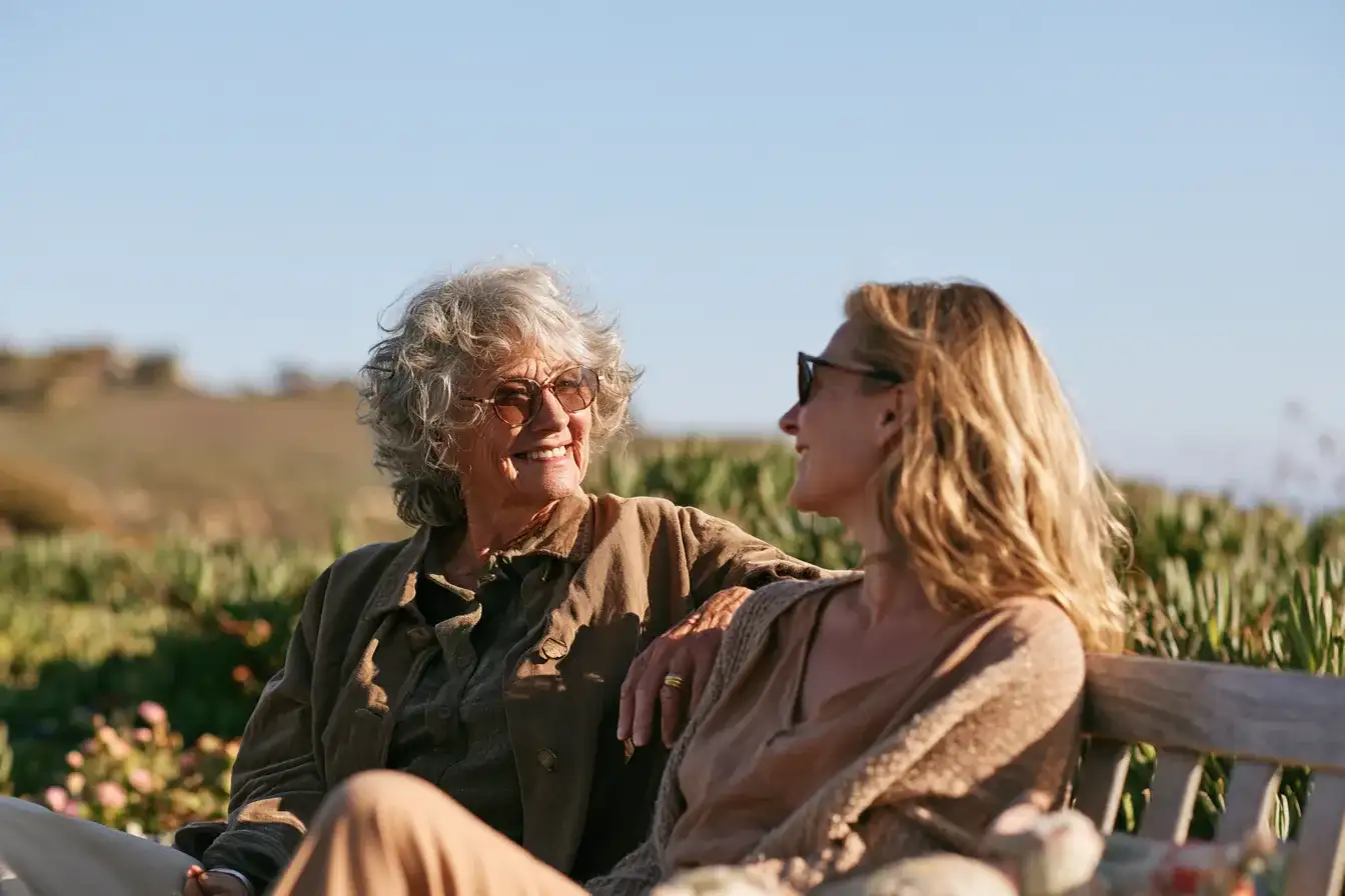 A mother in her seventies and daughter in her fifties talking on a garden bench