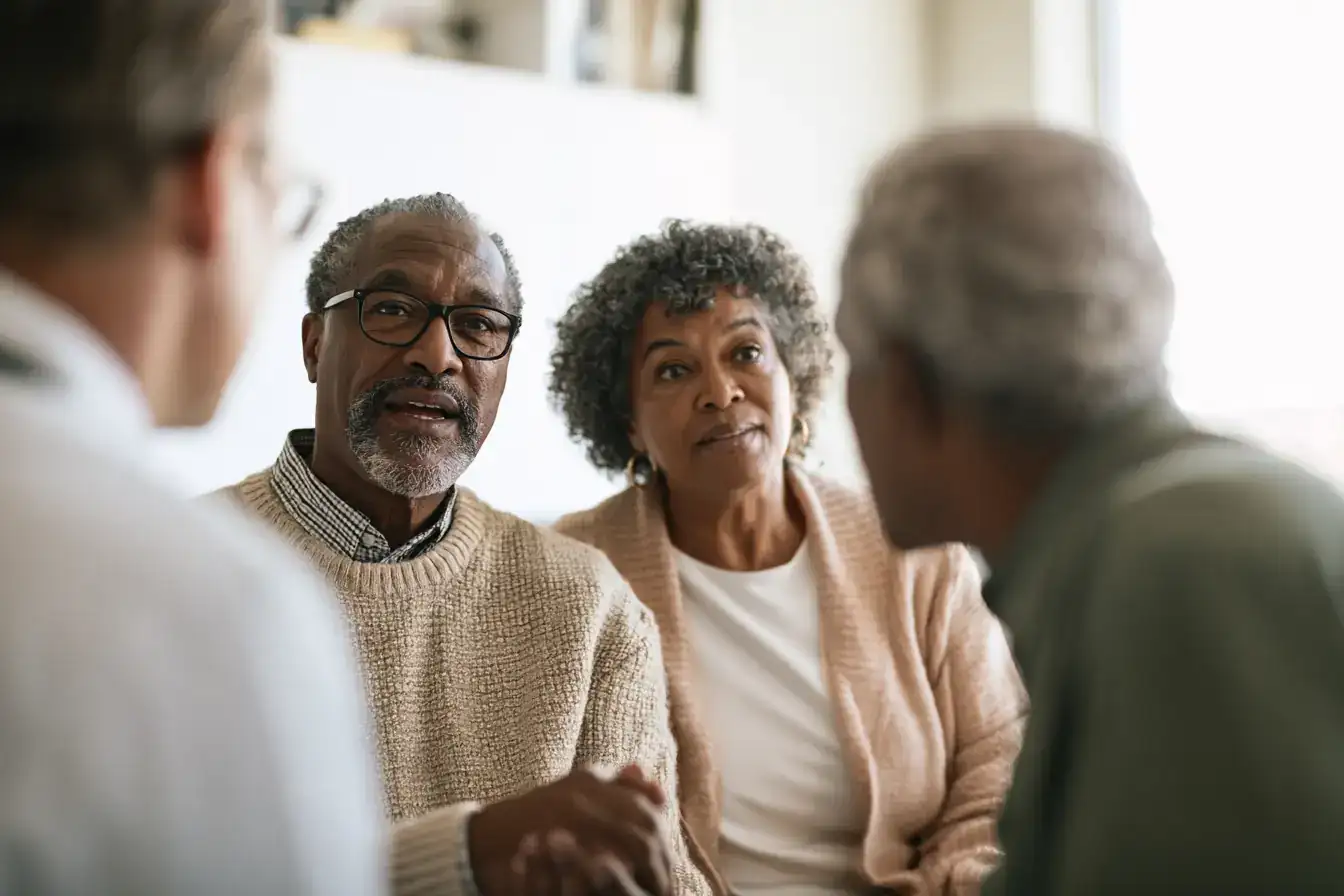 A Black man in his sixties and his wife watching a doctor turn a screen round to show something