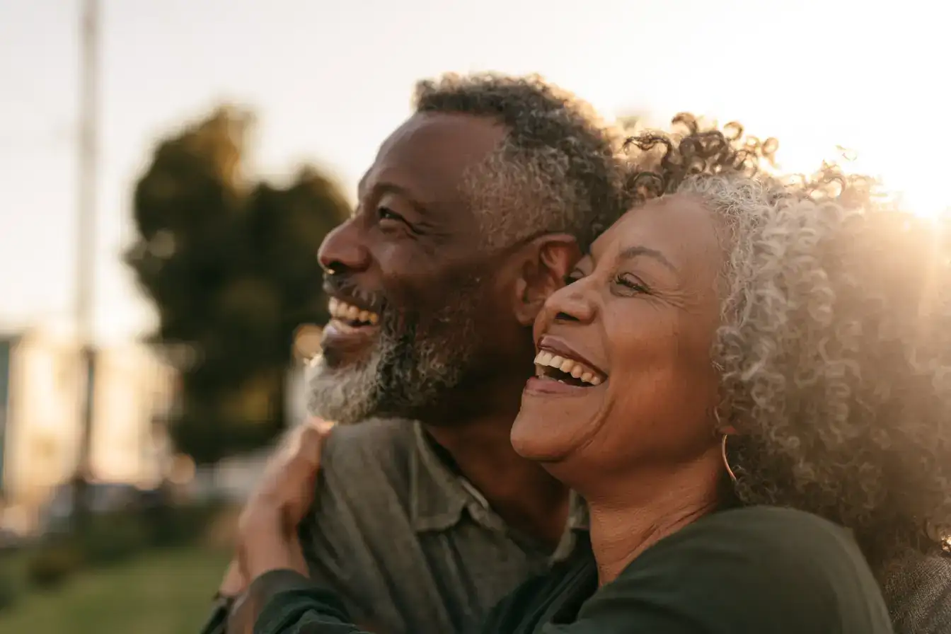 A Black man in his sixties and his wife laughing at something a grandchild just whispered