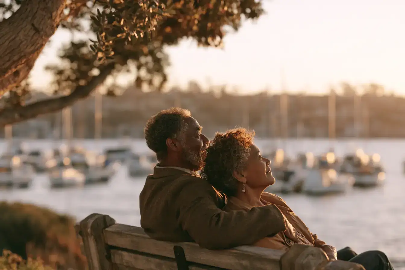 A Black man in his sixties and his wife sharing a bench, coffee cups between them