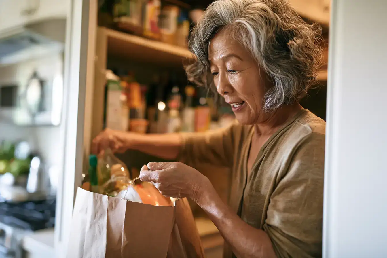 An Asian woman in her seventies picking herbs from a garden bed