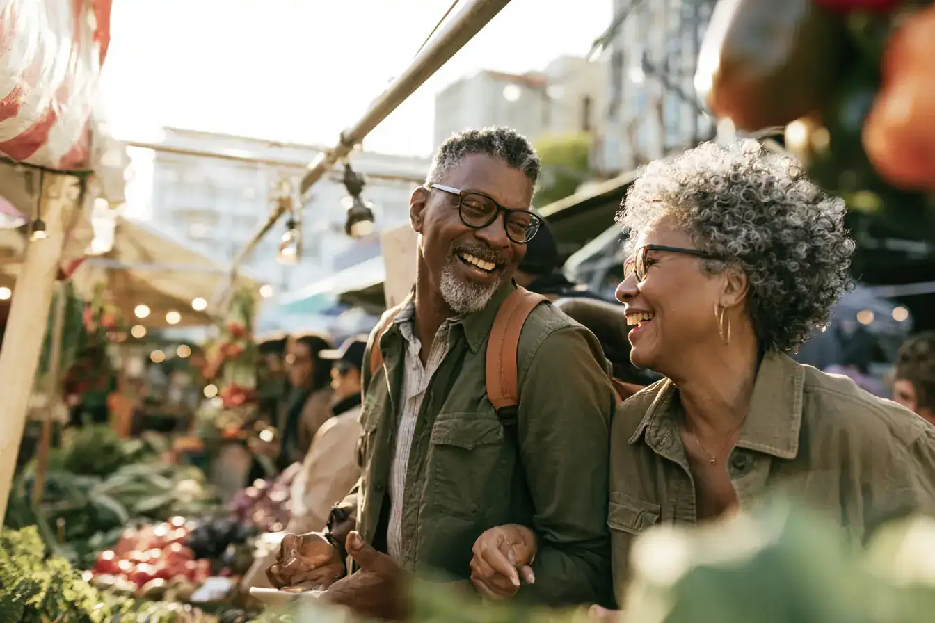 A Black man in his sixties and his wife catching up over the noise of a farmers market