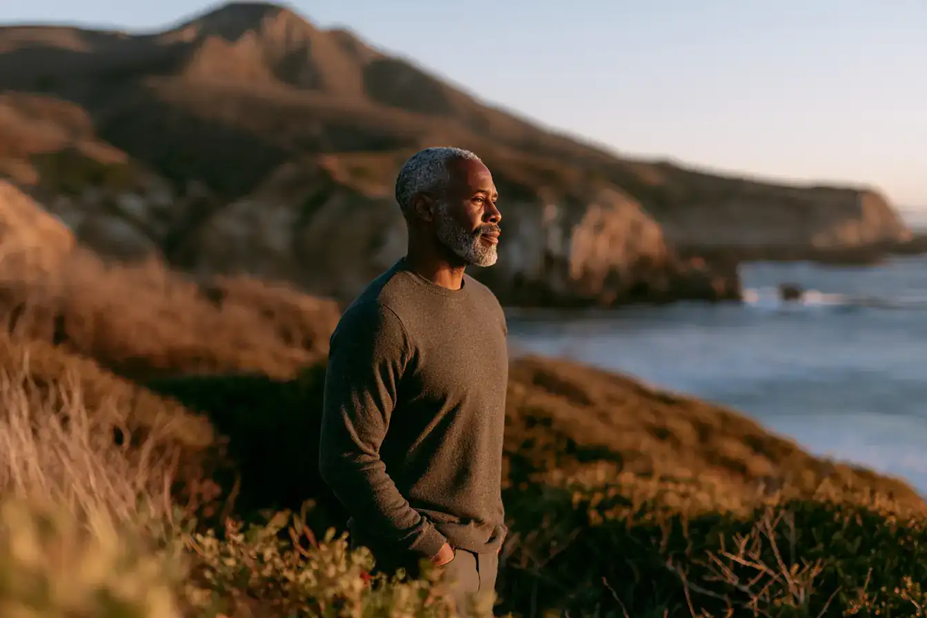 A Black man in his fifties hands in pockets on a long coastal walk