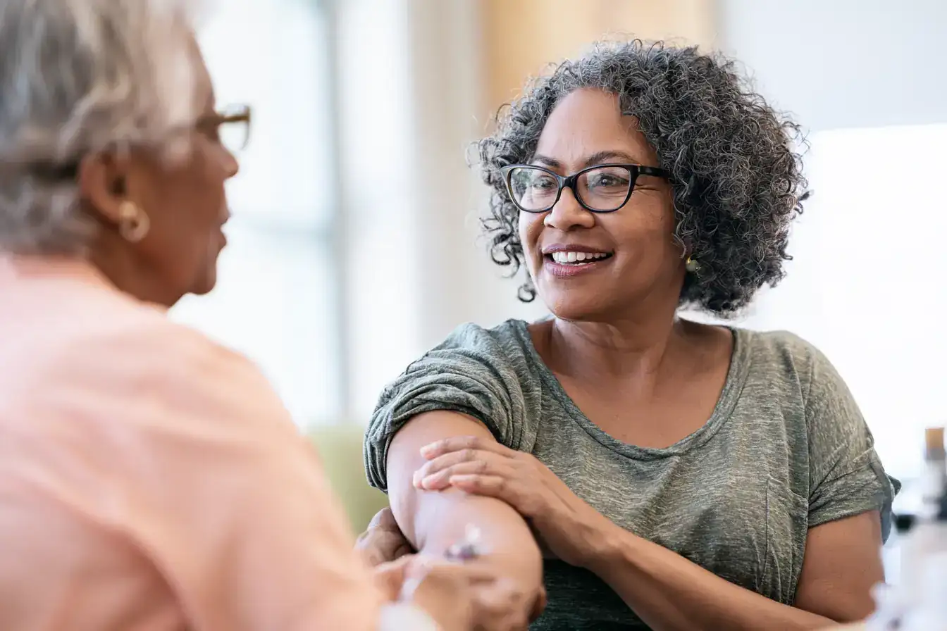 A Black woman in her fifties and her mother in her late seventies sharing a bench, coffee cups between them