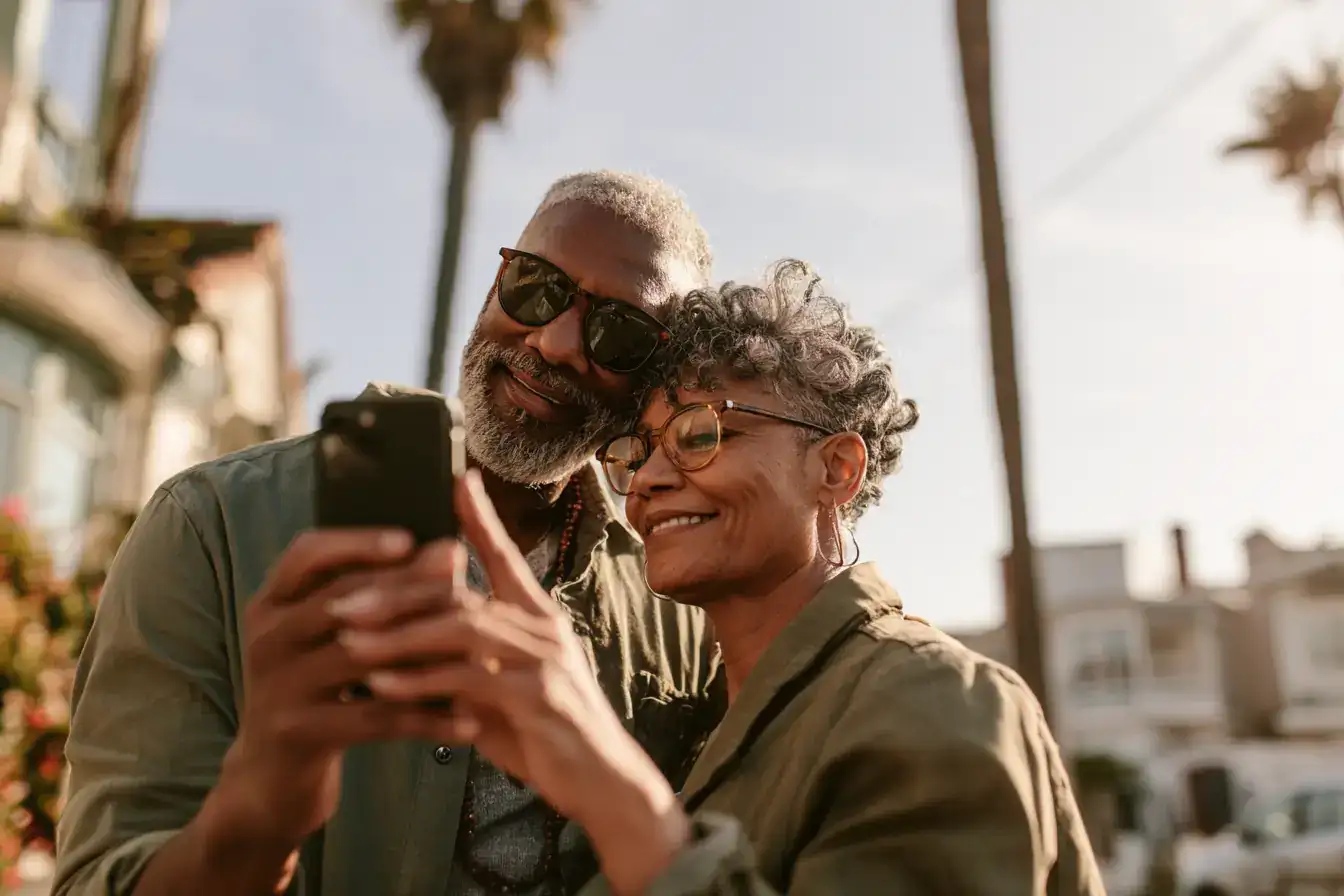A Black man in his sixties and his wife holding a phone up so both can see the screen
