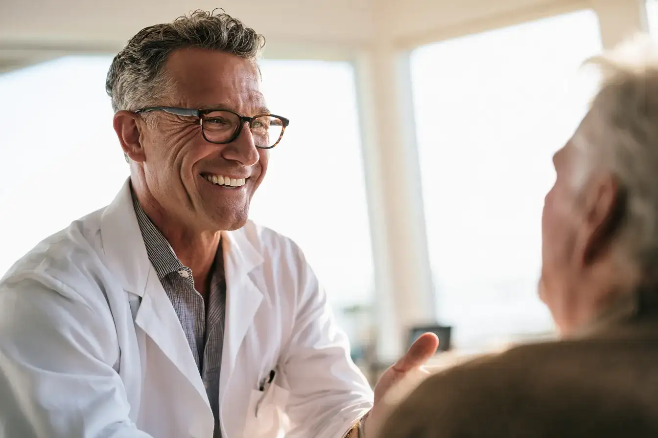 A neurologist in his fifties talking with an older patient in a bright consulting room