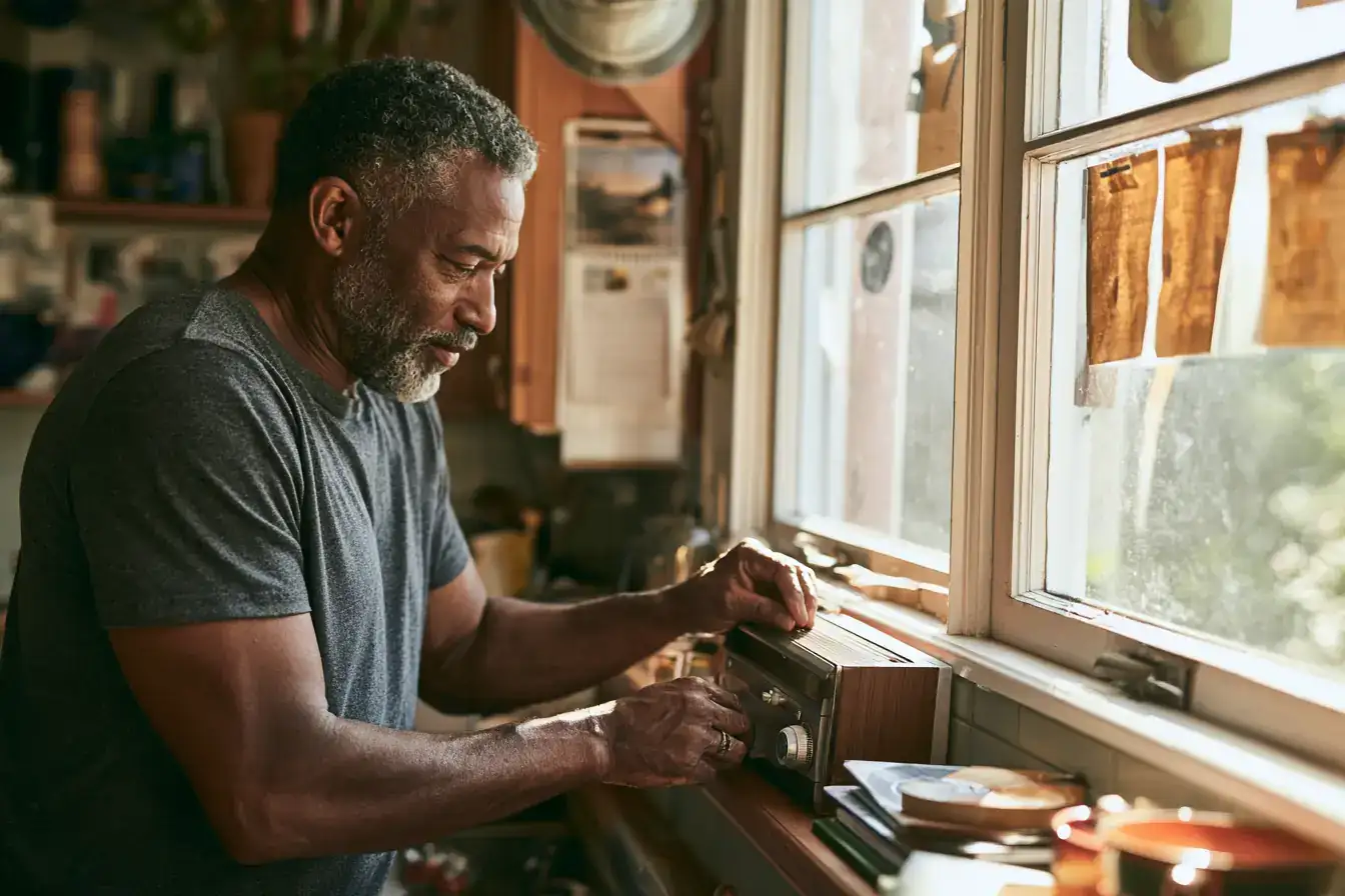 A Black man in his fifties tuning a radio on a kitchen windowsill